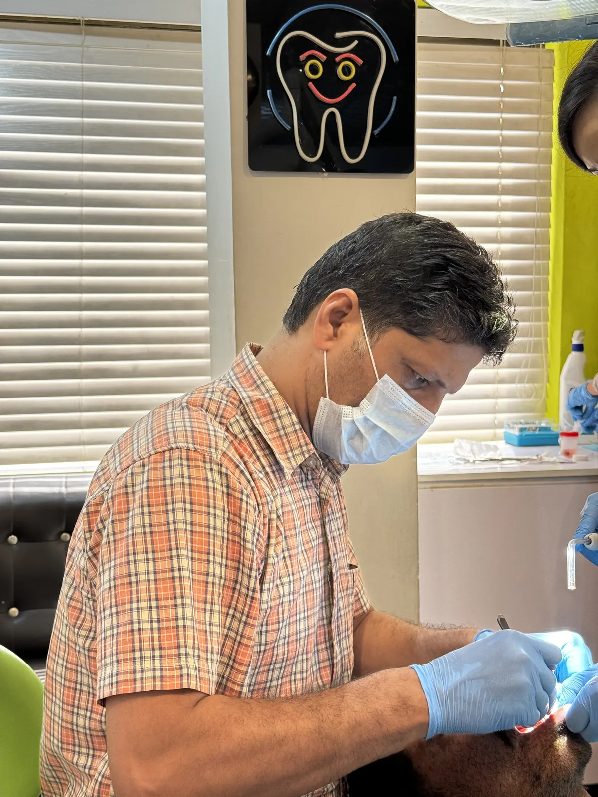Dr. Muhammad Jamal operating on a patient, under the practice's neon tooth sign.